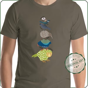 Puede incluir: Camiseta verde oliva con una ilustración vertical de cinco pájaros diferentes, cada uno con su nombre. Los pájaros son de varios colores, incluyendo azul, verde y marrón. Un sello circular "ORIGINAL ART" está a la derecha.