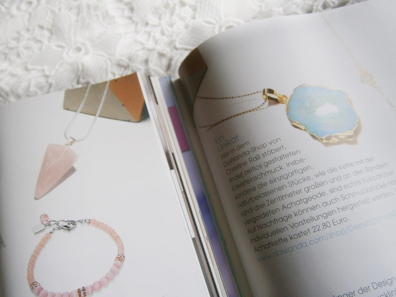 May include: A close-up of a light blue agate pendant necklace with a gold chain. The pendant is on a white surface with text about the necklace and the shop it is from. The text reads "Unikat der in dem DaWanda-Shop von Christine Ra&szlig; st&ouml;bert, indef zeitlos gestalteten Edelsteinschmuck. Insbe sondere die einzigartigen, naturbelassenen St&uuml;cke, wie die Katte mit der rund drei Zentimeter gro&szlig;en und an den R&ouml;nderm vergoldeten Achatgeode, sind echte Eyecatcher Auf Nachfrage k&ouml;nnen auch Schmuckst&uuml;cke nom individuellen Vorstellungen hergestel werden. Achatkette kostet 22,80 Euro. www.dawanda.com/shop/Deramick"