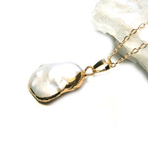 Könnte beinhalten: Eine goldene Kettenkette mit einem großen, unregelmäßig geformten weißen Perlenanhänger.
