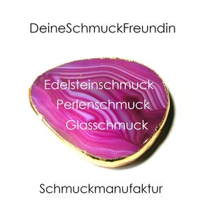 May include: A pink and white agate slice with a gold rim. The agate slice has the text "Edelsteinschmuck, Perlenschmuck, Glasschmuck" and "DeineSchmuckFreundin, Schmuckmanufaktur" written on it.