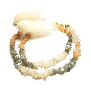 May include: A double-strand necklace made of light gray, white, and peach-colored gemstone chips. The necklace has a gold clasp.