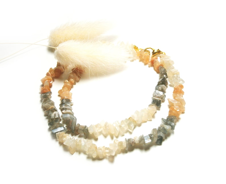 May include: A double-strand necklace made of light gray, white, and peach-colored gemstone chips. The necklace has a gold clasp.