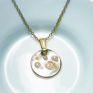 Vergoldete Gliederkette mit rundem, weißen Perlmuttanhänger mit eingeschlossenen kleinen Perlen. Der Perlmutt Anhänger ist am Rand umlaufend vergoldet und mit einer vergoldeten Anhängeröse an der Halskette befestigt.