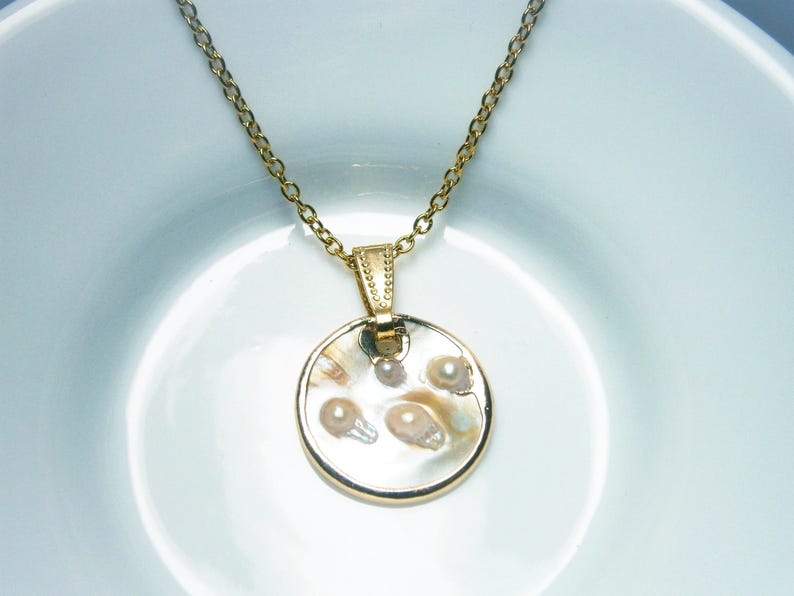 Vergoldete Gliederkette mit rundem, weißen Perlmuttanhänger mit eingeschlossenen kleinen Perlen. Der Perlmutt Anhänger ist am Rand umlaufend vergoldet und mit einer vergoldeten Anhängeröse an der Halskette befestigt.