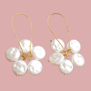 May include: A pair of gold hoop earrings with a cluster of five white pearl-like beads hanging from each hoop.