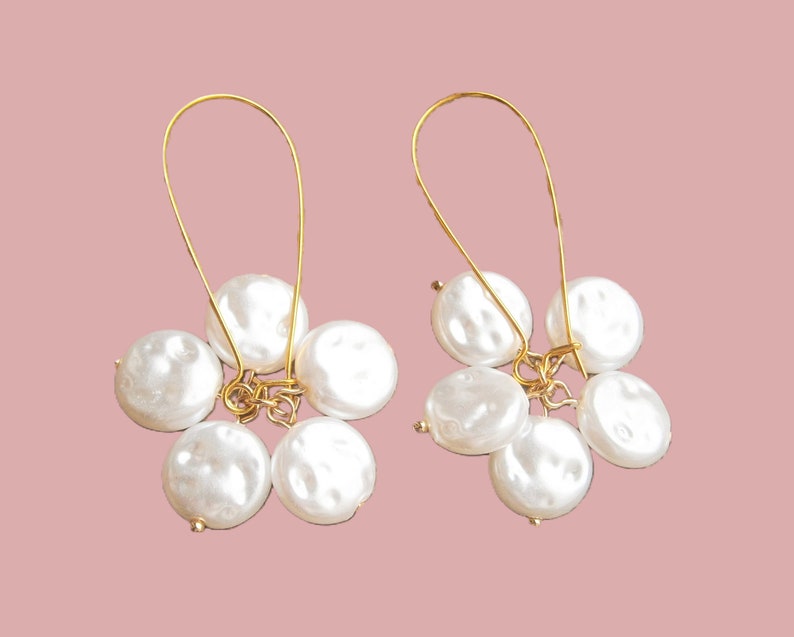 May include: A pair of gold hoop earrings with a cluster of five white pearl-like beads hanging from each hoop.