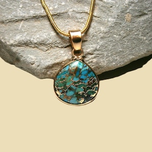 May include: A gold necklace with a teardrop pendant. The pendant has a mosaic of turquoise and brown-gold hues, set within a gold frame. The chain is a fine gold colour. The pendant is approximately 2.5 cm in length.