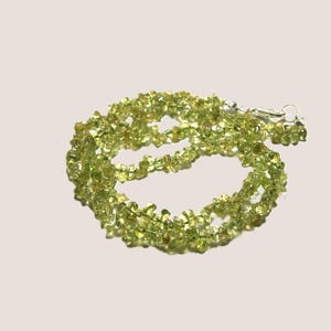 Könnte beinhalten: Eine Halskette bestehend aus zahlreichen kleinen, unregelmäßigen, durchscheinenden lindgrünen Peridot-Edelsteinsplittern, die aneinandergereiht sind. Die Kette verfügt über einen silberfarbenen Karabinerverschluss aus Metall für einen sicheren Halt.