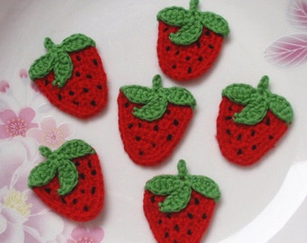 May include: Six red and green crocheted strawberry appliques on a white background.