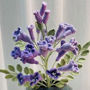 Op de afbeelding: Een boeket van gehaakte paarse bloemen met groene bladeren. De bloemen hebben de vorm van bellen en een delicaat, ingewikkeld ontwerp.