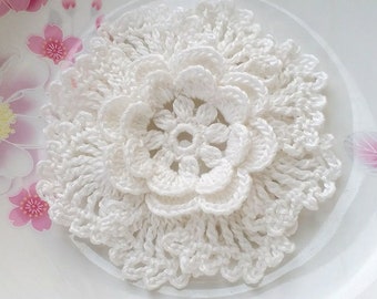 May include: A white crocheted flower with a delicate, lacy design. The flower has multiple layers of petals and a small center.
