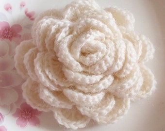 May include: A white crocheted flower with a delicate, layered design. The flower is made with soft yarn and has a fluffy texture.