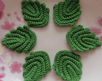 May include: Six green crocheted leaf shapes on a white plate with a floral pattern.