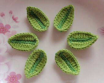 May include: Six green crocheted leaves with a light green center, arranged in a circle on a white plate with a floral pattern.