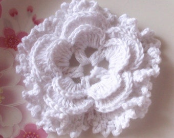 May include: A white crocheted flower with a ruffled edge. The flower is made with a delicate stitch pattern and has a center that is slightly raised.