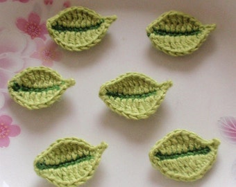 May include: Six crocheted green leaves with a darker green center, arranged on a white plate with a floral pattern.