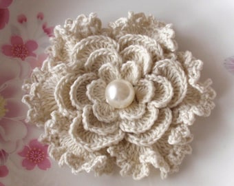 May include: A crocheted flower brooch in a cream color with a pearl in the center.