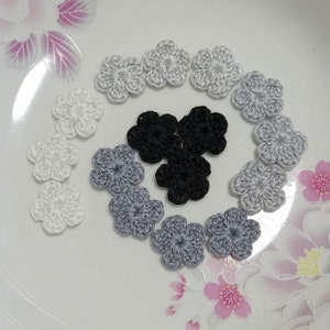 Può includere: Una collezione di fiori all'uncinetto in varie tonalità di grigio e nero. I fiori sono disposti in cerchio su uno sfondo bianco.