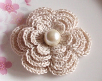 May include: A crocheted flower with a pearl center in a cream color.