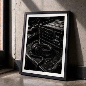 May include: A black and white framed print featuring a pair of over-ear headphones resting on a surface next to a crate filled with vinyl records. The crate has a label that reads VINYL IS FOREVER. A turntable is visible in the background.