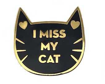 May include: Black and gold enamel pin shaped like a cat's head with the text "I miss my cat" inside.