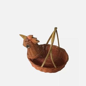 May include: A woven wicker basket shaped like a chicken with a brown and orange color scheme. The basket has a handle and is perfect for holding small items.
