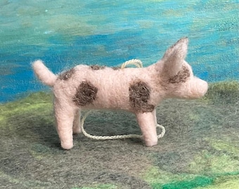 May include: A pink and brown spotted felt pig ornament. The pig is standing on all four legs and has a string attached to its neck.