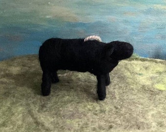 May include: A black felt sculpture of a cow standing on a green surface. The cow has a white rope around its neck.