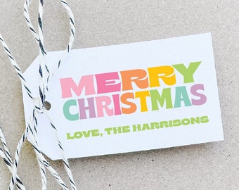 May include: A brown gift box with a white string tied around it. A white gift tag with the text "Merry Christmas" in colorful letters and "Love, The Harrisons" in green letters is attached to the string.