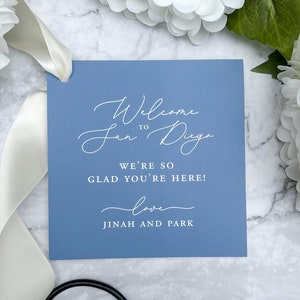 May include: A light blue welcome sign with white text that reads "Welcome to San Diego. We're so glad you're here! Love, Jinah and Park."