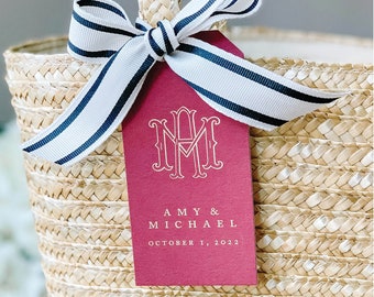 May include: A red gift tag with white lettering. The tag has a monogram of the letters "AM" with a heart in the middle. The text below the monogram reads "AMY & MICHAEL OCTOBER 1, 2022".