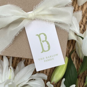 May include: A white gift tag with a green letter "B" in a decorative font. The text "THE BARLOW FAMILY" is printed below the letter.