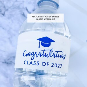 May include: Clear plastic water bottle with a white label. The label features a blue graduation cap graphic and the words "Congratulations CLASS OF 2027" in blue script. Text at the top reads "MATCHING WATER BOTTLE LABELS AVAILABLE".