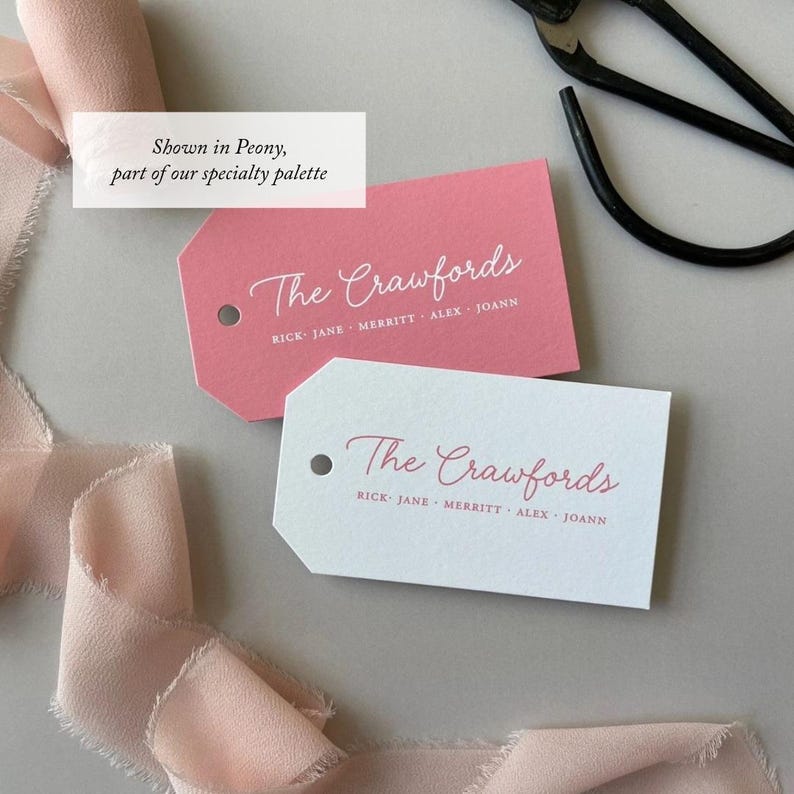 May include: Two rectangular paper gift tags with angled corners and a hole punch. One tag is pink with white text, the other is white with pink text. Both feature the script text The Crawfords and the names Rick, Jane, Merritt, Alex, Joann.