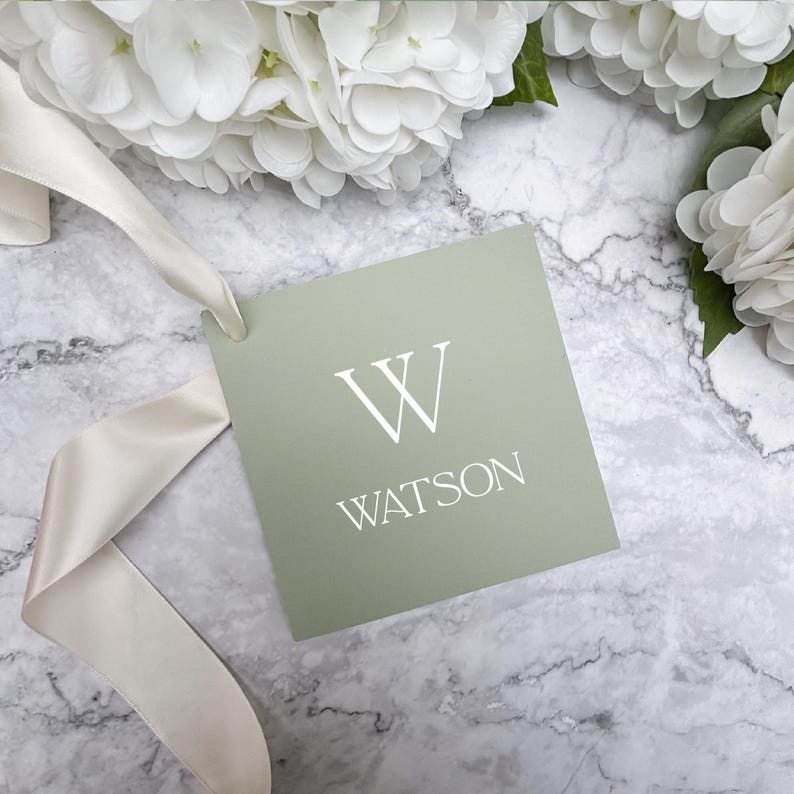 May include: A sage green gift tag with a white letter W and the name Watson printed in white.