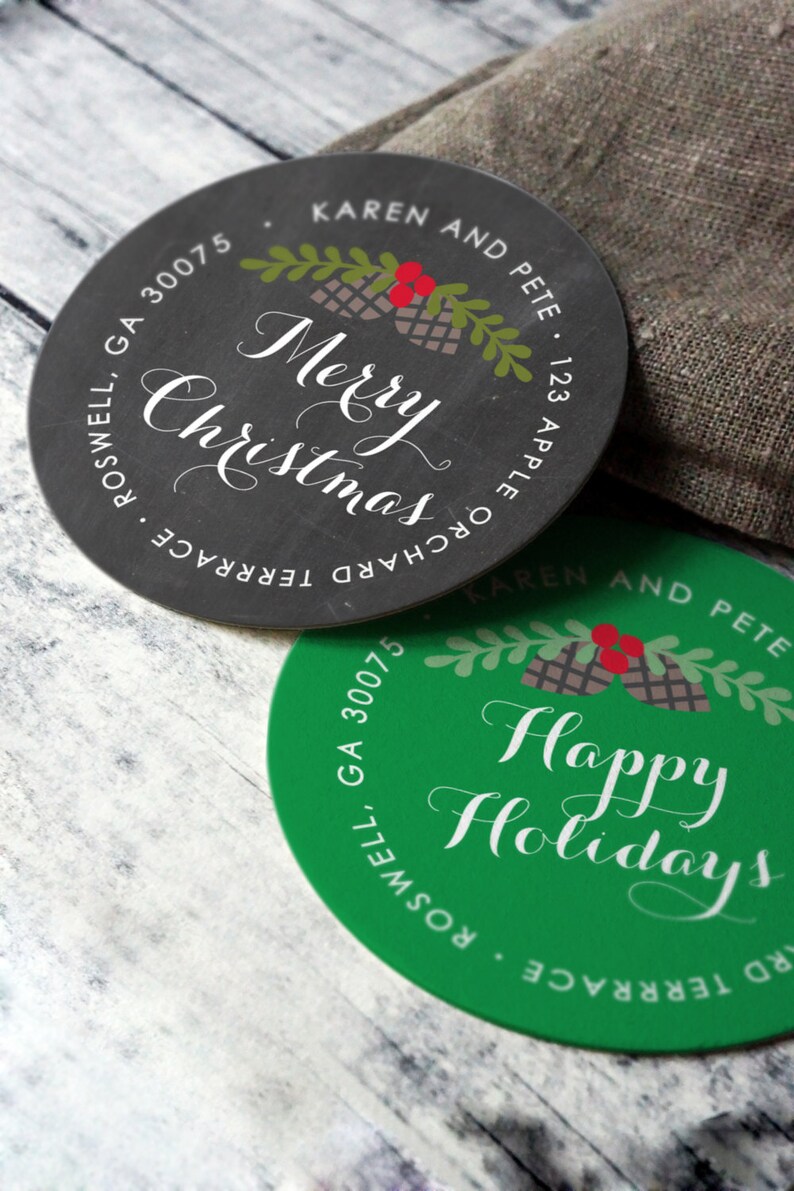 May include: Two round Christmas and holiday-themed stickers. One is black with "Merry Christmas" in white script, the other is green with "Happy Holidays" in white script. Both have festive illustrations and address details.