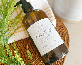May include: A brown glass bottle with a pump dispenser filled with dish soap. The bottle has a white label with the text "Baby Bottle Dish Soap The Essentials Highest Quality No. 242".