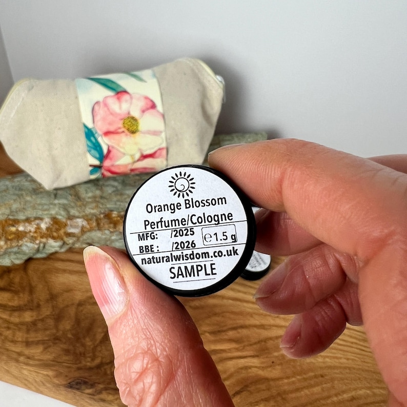 Pu&ograve; includere: Un piccolo barattolo di campione nero con un'etichetta bianca che recita "Orange Blossom Perfume/Cologne", "MFG: /2025", "BBE: /2026 e1.5 g", "naturalwisdom.co.uk" e "SAMPLE".