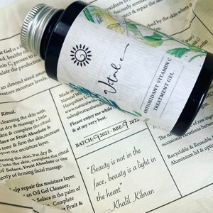 May include: A small, clear glass bottle with a black cap and a white label. The label has a sun graphic and the word "Vital" written in cursive. The bottle is sitting on a piece of paper with text about the product, including the quote "Beauty is not in the face, beauty is a light in the heart" - Khalil Gibran.