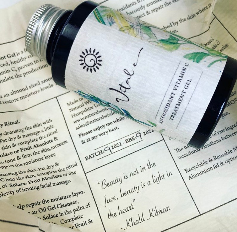 May include: A small, clear glass bottle with a black cap and a white label. The label has a sun graphic and the word "Vital" written in cursive. The bottle is sitting on a piece of paper with text about the product, including the quote "Beauty is not in the face, beauty is a light in the heart" - Khalil Gibran.
