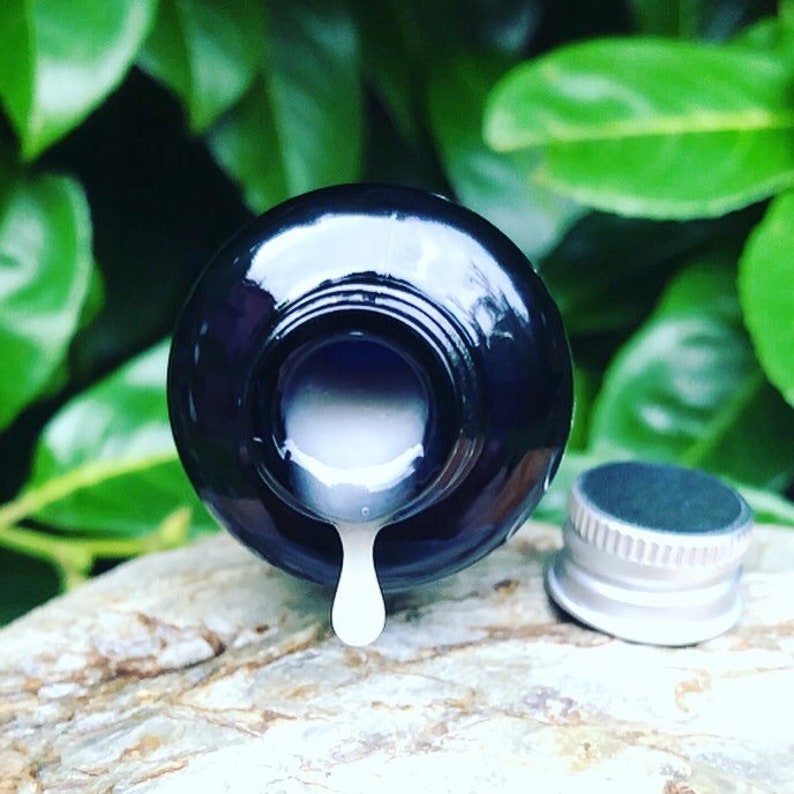 May include: A dark blue glass bottle with a silver lid, pouring a white liquid onto a textured surface. The bottle is upside down, and the liquid is dripping from the opening.