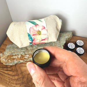 Pu&ograve; includere: Un set di piccoli barattoli di campioni di miscele di oli essenziali naturali. I barattoli sono etichettati con i nomi delle miscele: "Amber Vanilla", "Sandlewood & Cedarwood" e "Rose & Frankincense". I barattoli sono posizionati su un pezzo di legno con una borsa di tela con motivo floreale sullo sfondo.