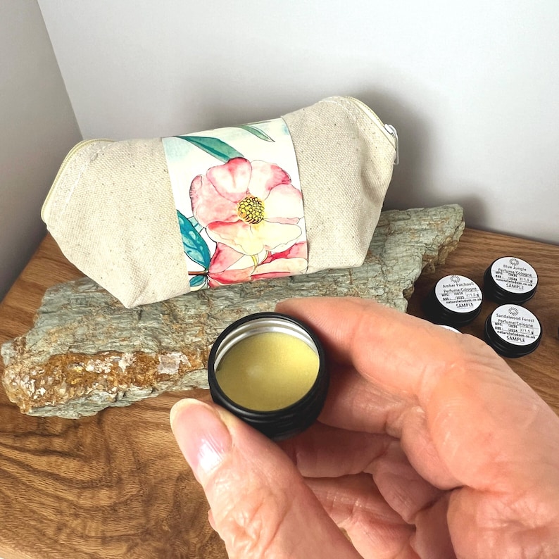 Pu&ograve; includere: Un set di piccoli barattoli di campioni di miscele di oli essenziali naturali. I barattoli sono etichettati con i nomi delle miscele: "Amber Vanilla", "Sandlewood & Cedarwood" e "Rose & Frankincense". I barattoli sono posizionati su un pezzo di legno con una borsa di tela con motivo floreale sullo sfondo.