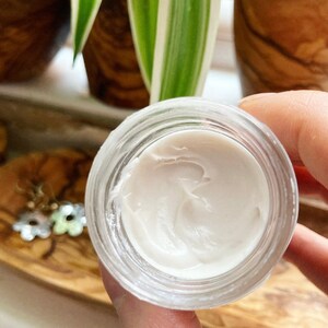 May include: A small glass jar with a white, creamy substance inside. The jar is clear and has a smooth, rounded edge.