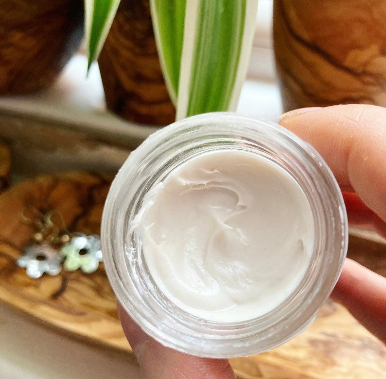 May include: A small glass jar with a white, creamy substance inside. The jar is clear and has a smooth, rounded edge.
