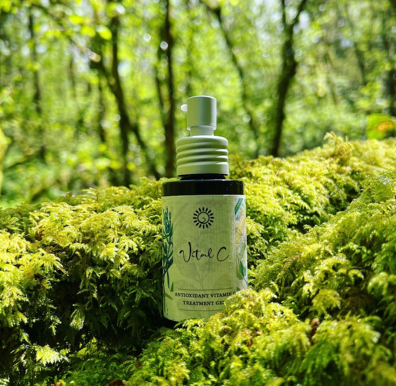 May include: A small bottle of Vital C Antioxidant Vitamin C Treatment Gel, with a white pump top, sitting on a bed of green moss. The bottle has a white label with a sun and flower design.