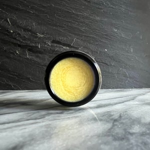 May include: A black jar with a yellow, swirling, creamy substance inside.