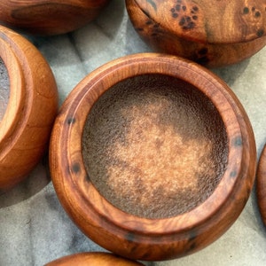 A cedar wood jar pod with unique knotted grain approximately 5cm in diameter & 3cm in hight, hand made from the root wood of the African Cedar tree displays its contents of Amber solid natural perfume. A warm, exotic honey & caramel fragrance