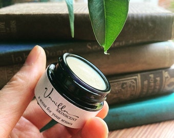 May include: A small, round jar of vanilla scented skin balm with a black lid and a white label that reads "Vanilla SKINScent a scent for your senses".