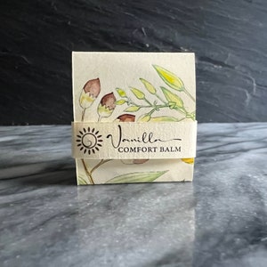 May include: A small, rectangular box with a white background and a floral design. The box has a label that says "Vanilla Comfort Balm".